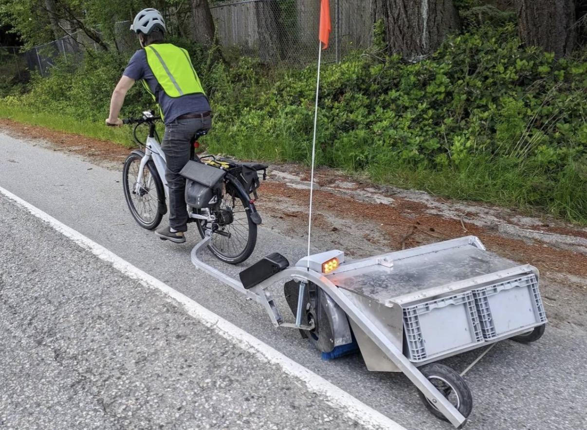 Agent de Cleaning Bio à vélo utilisant une Bike Lane Sweeper, une remorque-balayeuse conçue pour le nettoyage des pistes cyclables.