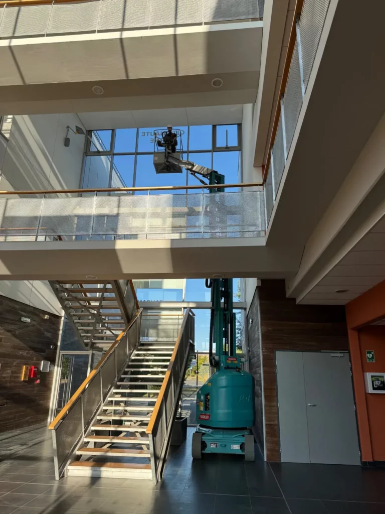 Intervention professionnelle de nettoyage de vitres en hauteur à l’aide d’une nacelle articulée dans un bâtiment tertiaire.