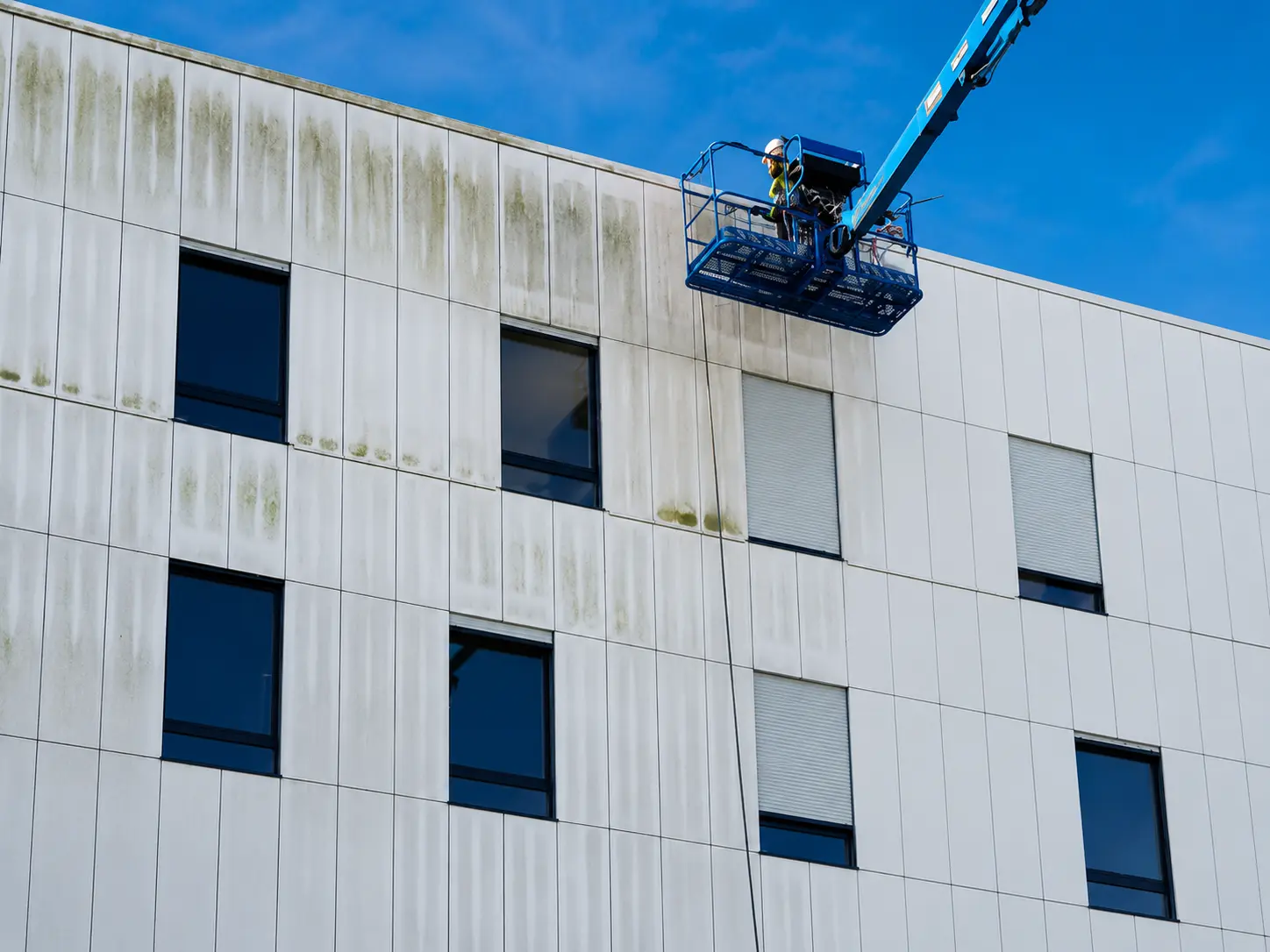 Agent Cleaning Bio nettoyant en hauteur la façade extérieure d’un bâtiment professionnel qui jouxte une copropriété et ce, à l’aide d’une nacelle