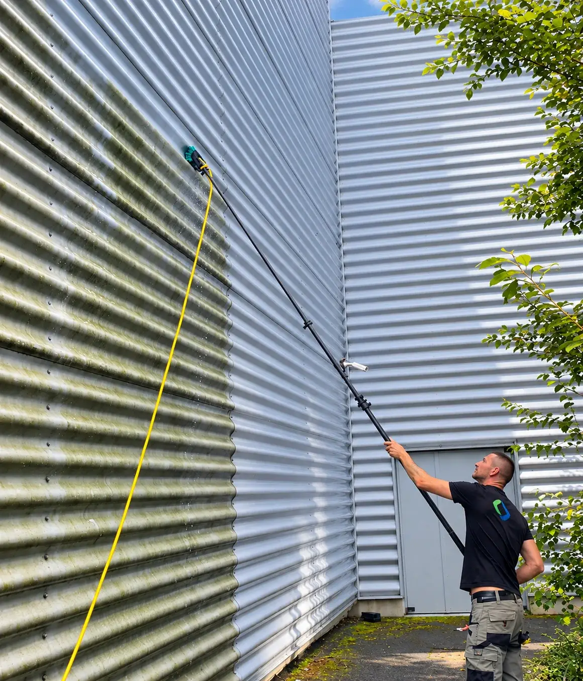 L'image montre professionnel Cleaning Bio en train de nettoyer la façade d'un bâtiment industriel à l'aide d'un équipement haute pression.