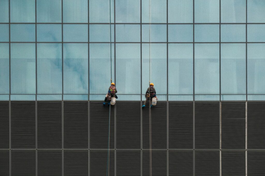 Two window cleaners suspended on ropes cleaning a modern skyscraper facade.